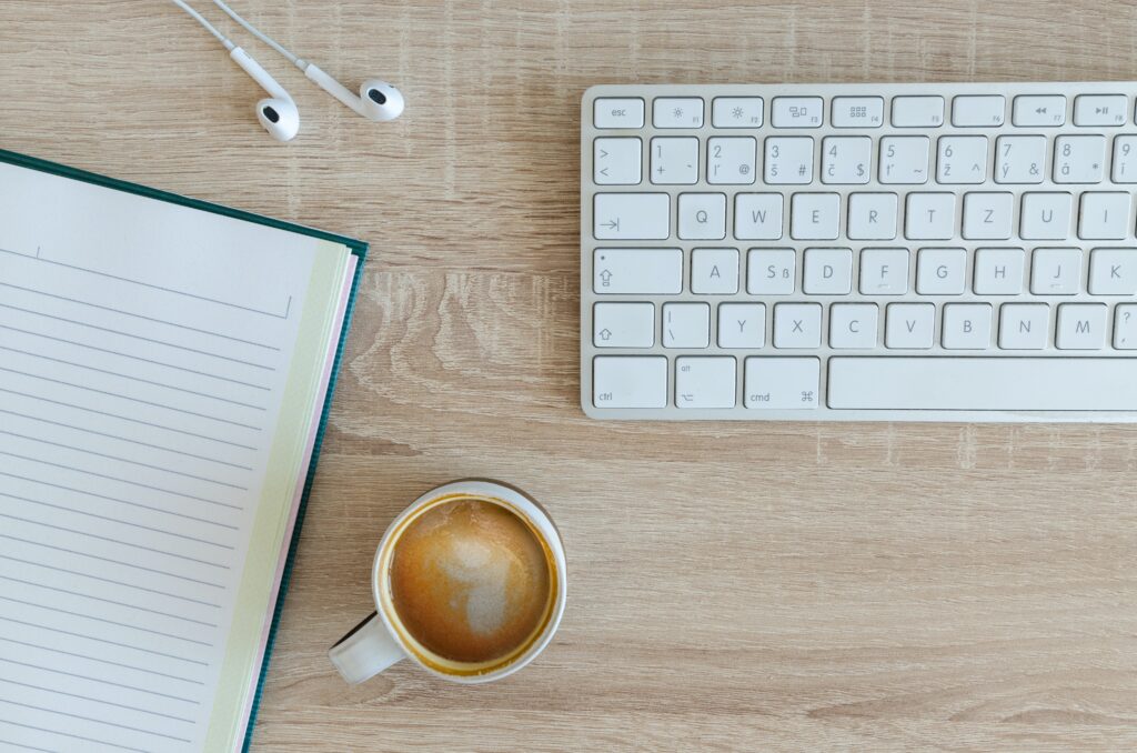 Notebook, earbuds, coffee and keyboard are featured in this image.